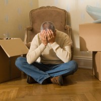 mid adult man sitting on a hardwood floor and suffering from a headache - home decoration stock pictures, royalty-free photos & images
