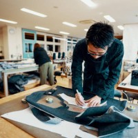 mid adult tailor cutting denim around a pattern in preparation to make a pair of jeans - fashion stock pictures, royalty-free photos & images