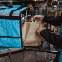 midsection of delivery man putting package order in backpack outside deli store - junk food stock pictures, royalty-free photos & images
