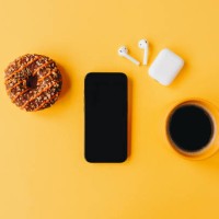 minimalistic breakfast scene with coffee, a chocolate donut, and smartphone on a bright yellow background - junk food stock pictures, royalty-free photos & images