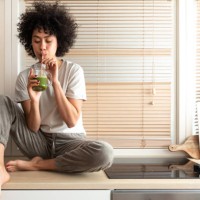 mixed race black latina woman drinking healthy green juice sitting on kitchen counter. copy space. healthy eating. - food stock pictures, royalty-free photos & images