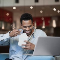 mixed race businessman using laptop and eating chinese food in living room - junk food stock pictures, royalty-free photos & images
