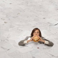 mixed race businesswoman drowning in paperwork eating hamburger - junk food stockfoto's en -beelden