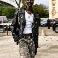 Model is seen wearing a black biker jacket, white Loewe shirt, cargo pants and black and silver chain bag outside the Chanel show during the...