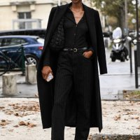 Model is seen wearing a black biker overcoat, black shirt, black striped pants and black belt with a black bag outside the Chanel show during the...