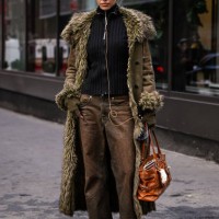 Model is seen wearing a green faux fur coat, black sweater, brown jeans and tan bag with brown headphones outside the Lapointe show during NYFW F/W...