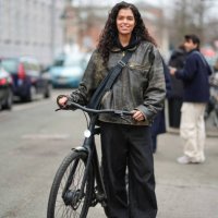 Model wears a leather jacket, crossbody bag, black flared pants , leather shoes , uses a bike / bicycle, outside Lovechild 1979, during the...