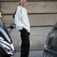 Model wears a white fluffy pullover, a bag, black flared pants, sneakers, outside Victoria Beckham, during the Womenswear Spring/Summer 2024 as part...