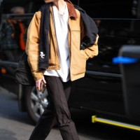 Model wears a white t-shirt, a beige leather jacket, a scarf, a black white and yellow cap, black pants, black leather shoes, outside Onitsuka Tiger...