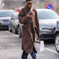 Model wears black sunglasses, silver earrings, dark brown wool oversized coat, a gold ring, black crossbody leather bag, dark navy blue lose denim...