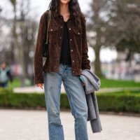 Model wears black t-shirt, dark brown suede jacket, shiny black leather bag, light blue denim jean pants, shiny black loafer moccasin leather shoes,...