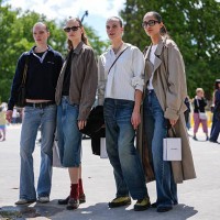 Model wears black t-shirt, navy blue long sleeve Miu Miu sweeter, shiny black leather bag, black leather belt, navy blue washed denim jean pants,...