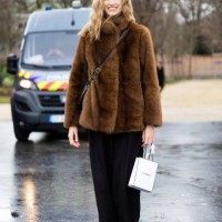 Model wears black trousers, brown heeled leather ankle boots, a black leather cross-body bag and a brown fur jacket outside Chanel during Haute...