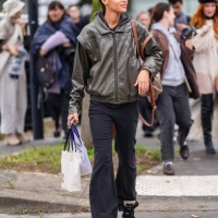 Model wears dark brown leather bomber jacket, black fitted pants, dark brown leather bag, outside Chloe, during the Paris Fashion Week Spring/Summer...