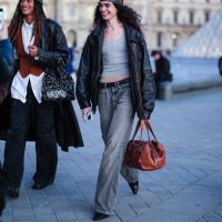 Model wears dark gray pattern head scarf, day gray tank top, shiny black oversized leather jacket, black leather belt, washed dark gray denim jean...