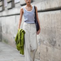 Model wears white and light blue striped tank top, white denim jean loose pants, bright green jacket in hand, dark brown leather bag, white boots...