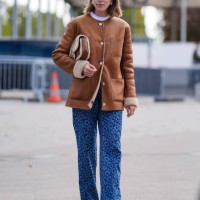 Monica Ainley wears gold earrings, white t-shirt, dark brown suede coat with gold buttons, light brown dark brown quilted Chanel leather bag, dark...