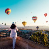 mooie aziatische vrouw kijken kleurrijke hete lucht ballonnen vliegen over de vallei in cappadocië, turkey.turkey cappadocië sprookjesachtige landschap van bergen. turkije cappadocië sprookjesachtige landschap van bergen. - t