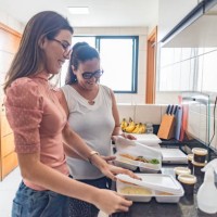 mother and adult daughter unpacking take-away food on the kitchen counter - junk food stock pictures, royalty-free photos & images