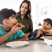 mother and young boys eating pizza in kitchen - junk food stock pictures, royalty-free photos & images