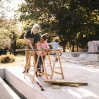 mother cutting wood with hand saw by daughter outside house - home decoration stockfoto's en -beelden