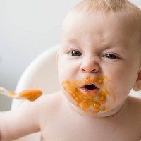mother feeding messy baby son with spoon in high chair - food stock pictures, royalty-free photos & images
