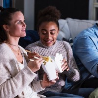 multi-ethnic family on couch watching tv, eating takeout - junk food stock pictures, royalty-free photos & images