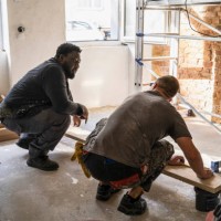 multiracial male carpenters crouching in front of plank while in apartment - home decoration stock pictures, royalty-free photos & images
