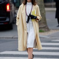Natasha Goldenberg wears white blouse, white midi skirt, yellow coat, brown heels, black leather gloves, white sunglasses, outside Miu Miu, during...