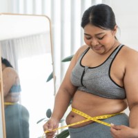 nice chubby woman measuring her waist while standing in front of the mirror - junk food stock pictures, royalty-free photos & images