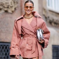 Nina Sandbech wears light brown sunglasses, gold earrings, gold chain necklace, sand beige oversized blazer belted mini trench dress, white and black...
