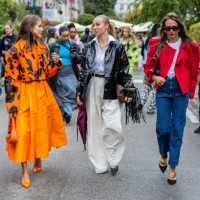Nina Sandbech wears orange black cow print cropped jacket, pleated skirt, bag, heels Prada & Sandra Hagelstam wears vinyl jacket, wide leg pants &...