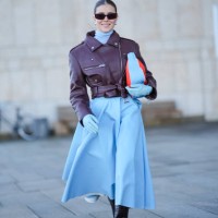 Nina Suess wears sunglasses , a blue turtleneck long gathered oversized dress, a purple leather biker jacket , a red and blue bag, black leather...