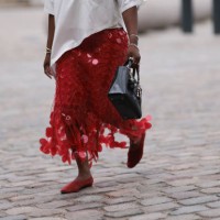 Nnenna Echem is seen wearing a white asymmetric round-necked t-shirt with wide sleeves; several silver bangles and rings; a knee-length red skirt...