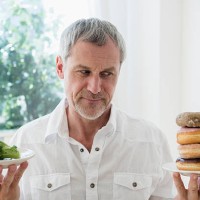 older caucasian man choosing between broccoli and donuts - junk food stock pictures, royalty-free photos & images