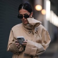 Olga Sokolenko seen wearing black sunglasses, gold / silver hoop earrings, 1811 Eighteen One One beige short trench coat with a bow detail and Rhode...
