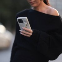 Olga Sokolenko seen wearing Say No More black off-shoulder asymmetrical oversized cotton sweater and Rhode grey silicone lip phone case, during the...