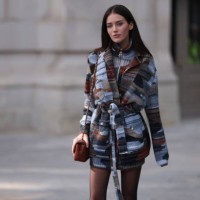 Olivia Neill is seen wearing a blue and brown patterned sweater with a turtleneck, a matching wool jacket and belt, high black boots and a brown...