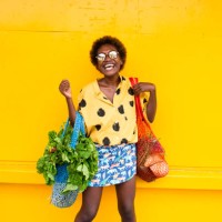 one young woman carrying grocery bags in front of yellow wall laughing - fashion stock pictures, royalty-free photos & images