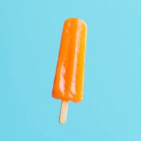 orange flavoured and colored popsicle stick on blue/turquoise background - junk food stock pictures, royalty-free photos & images