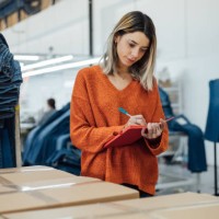 ouvrière prenant des notes sur la boîte de vêtements dans l’usine - fashion photos et images de collection