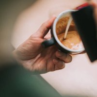 over the shoulder asian chinese male barista pouring froth milk on coffee cup prepared coffee latte art at bar counter - coffee stock pictures, royalty-free photos & images