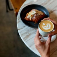 over the shoulder view of an asian woman enjoying her breakfast, a croissant with a cup of coffee in a cafe during the morning - coffee stockfoto's en -beelden