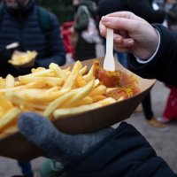 over the shoulder view of woman eating chips and curry sausage from a paper tray at a german christmas market. - junk food stock pictures, royalty-free photos & images