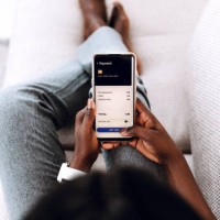 over the shoulder view of young black woman making order in cafe with smartphone sitting on the sofa at home. - junk food stock pictures, royalty-free photos & images