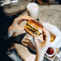over the shoulder view of young woman enjoying her meal, eating a freshly made beef and cheese burger with fries and having a glass of iced milkshake in a restaurant - junk food stock pictures, royalty-free photos & images