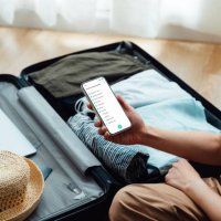over the shoulder view of young woman looking at checklist on smartphone while packing luggage - travel stock pictures, royalty-free photos & images