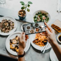 overhead view of a woman's hand taking photo of freshly served food before eating it with smartphone in a restaurant - food stock pictures, royalty-free photos & images