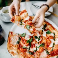overhead view of woman's hand getting a slice of freshly made pizza and enjoying her meal in an italian restaurant - junk food stock pictures, royalty-free photos & images