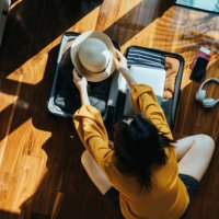 overhead view of young asian woman sitting on the floor in her bedroom, packing a suitcase for a trip. getting ready for a vacation. traveller's accessories. travel and vacation concept - travel stock pictures, royalty-free p